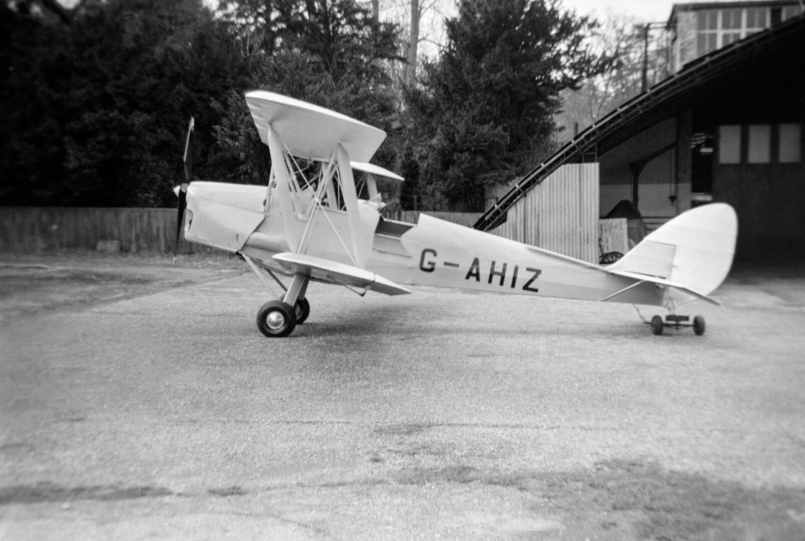 2DKDW6X A vintage black and white photograph taken in 1954 showing a De Havilland Tiger Moth aeroplane, registration G-AHIZ, parked outside of a hangar in England.